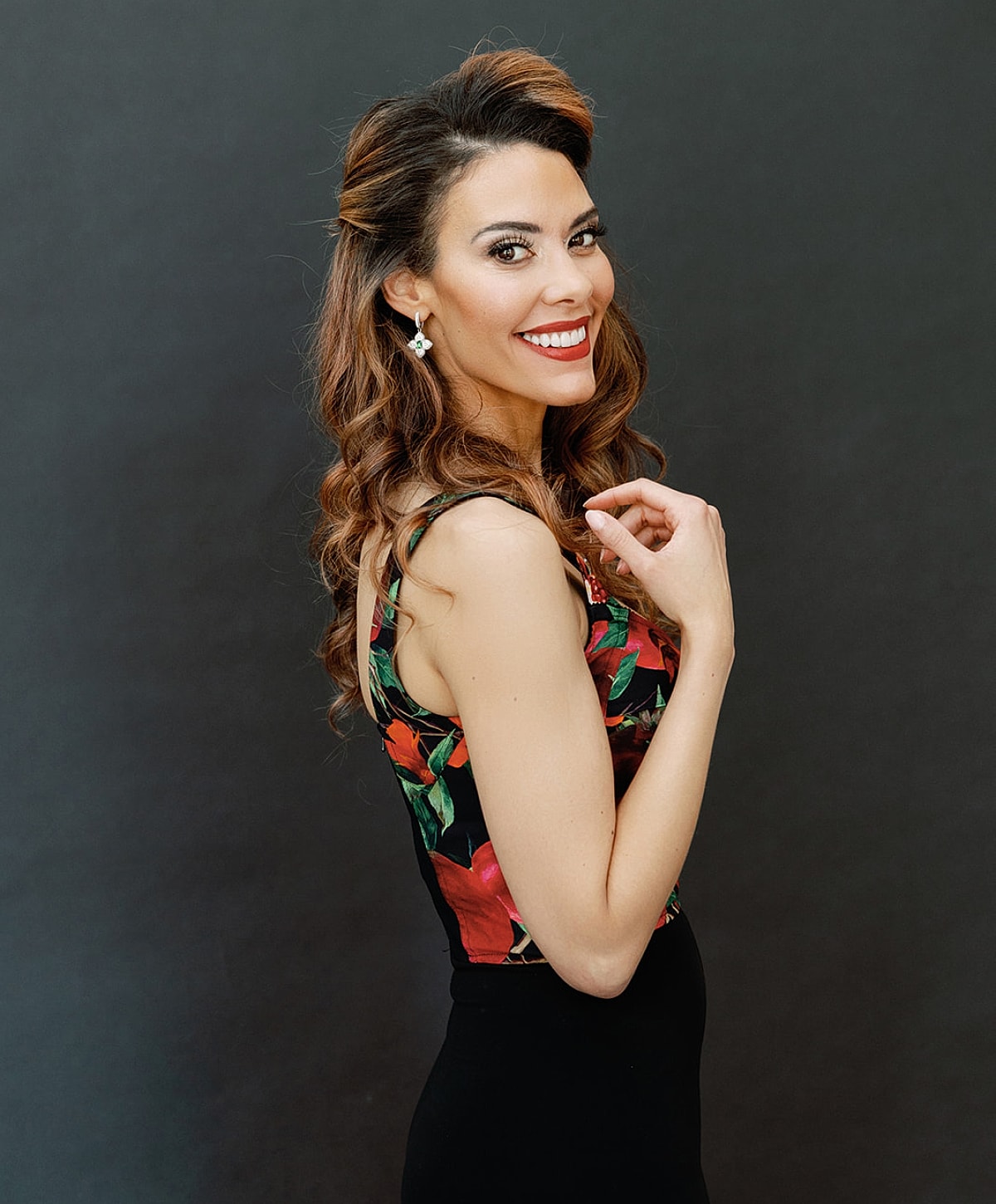 Woman smiling in floral outfit against dark background.