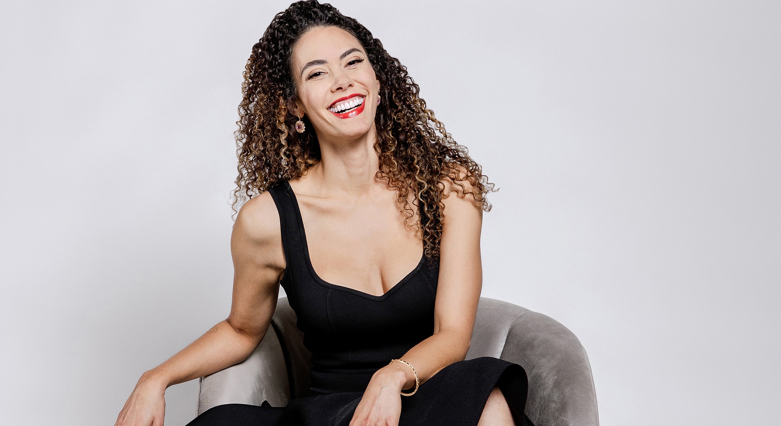 Smiling woman with curly hair in black dress.